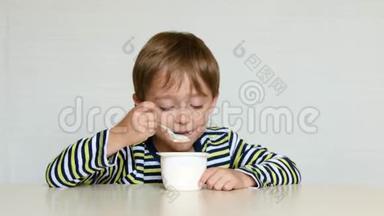 男孩坐在桌子旁，从罐子里吃酸奶，体验情绪：快乐、快乐、快乐。 儿童食品